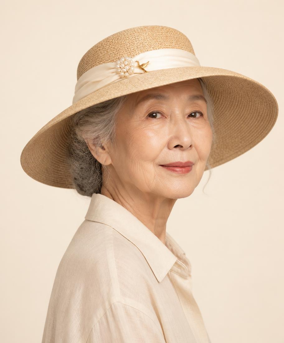 Elegant Japanese grandmother in a cream linen shirt wearing a wide-brim straw hat with ivory silk ribbon, pearl cluster and a gold crane charm