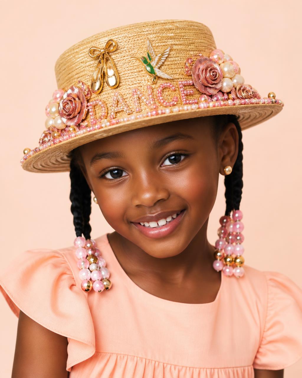 Eight year old Black girl with beaded braids in a peach dress wearing a straw boater bedazzled with pink beaded lettering, pearl clusters, gold ballet slipper charm and a hummingbird